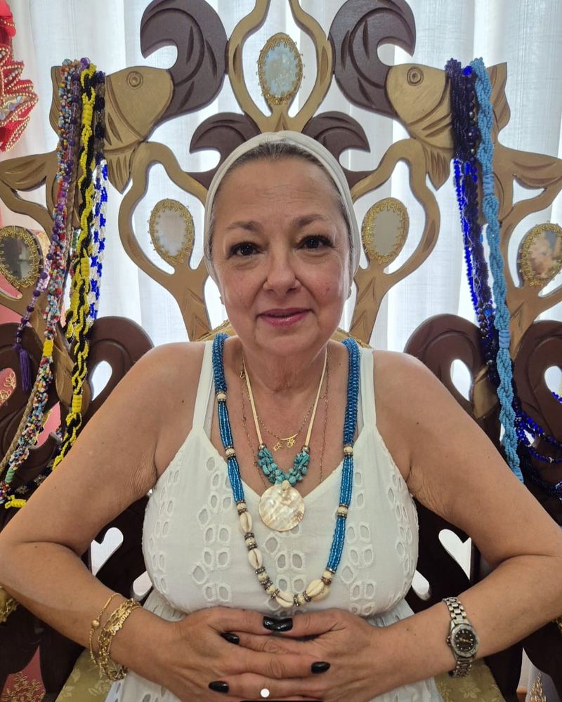 Mãe Dalva de Iemanjá, sacerdotisa espiritual, sorrindo com colar de contas azuis, símbolo de Iemanjá