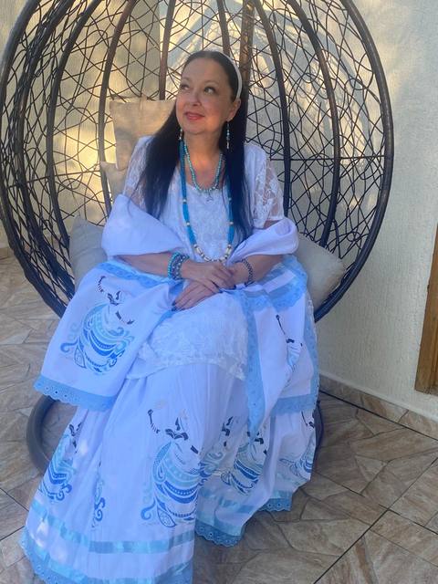 Mãe Dalva sorridente, vestida de branco e azul-turquesa