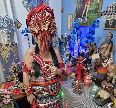 Mãe Dalva em vestido vermelho, junto ao altar iluminado